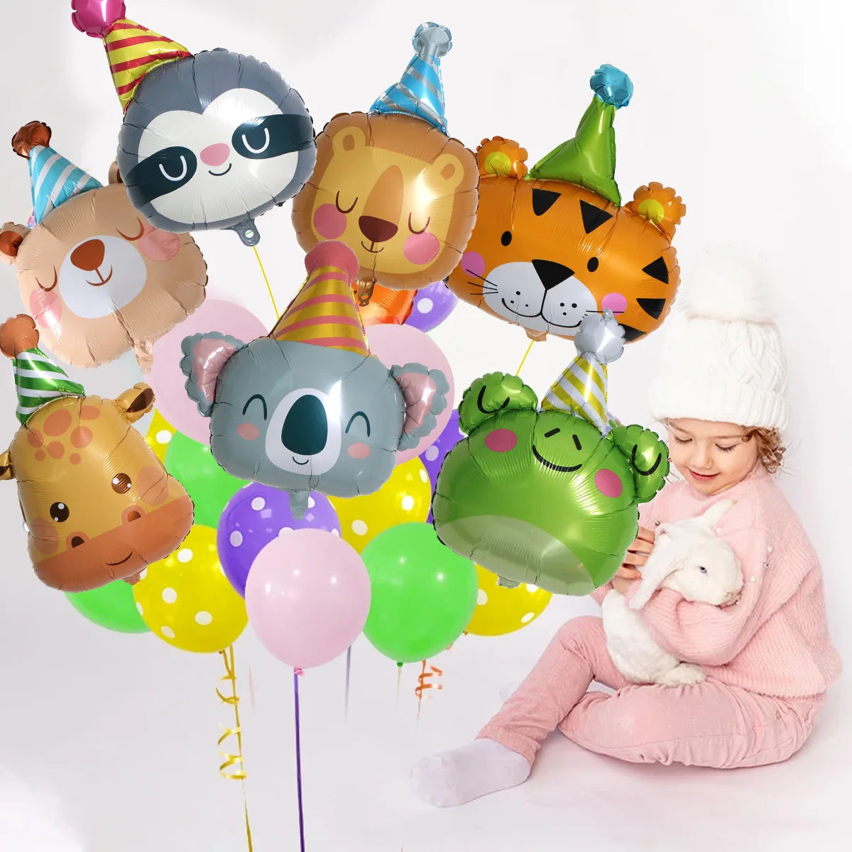 A child is sitting and holding a white rabbit while surrounded by various jungle animal foil balloons.
