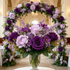 A lush bouquet of artificial mixed flowers featuring purple and lavender roses, daisies, and chrysanthemums displayed on a wh