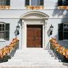 A white clapboard house entrance decorated with autumn maple leaf garlands on the steps and around the doorway.