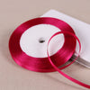 A roll of vibrant magenta satin ribbon on a white spool, ready for gift wrapping or crafts.