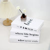 A set of three white decorative fake books with text on them, resting next to a vase of white flowers.
