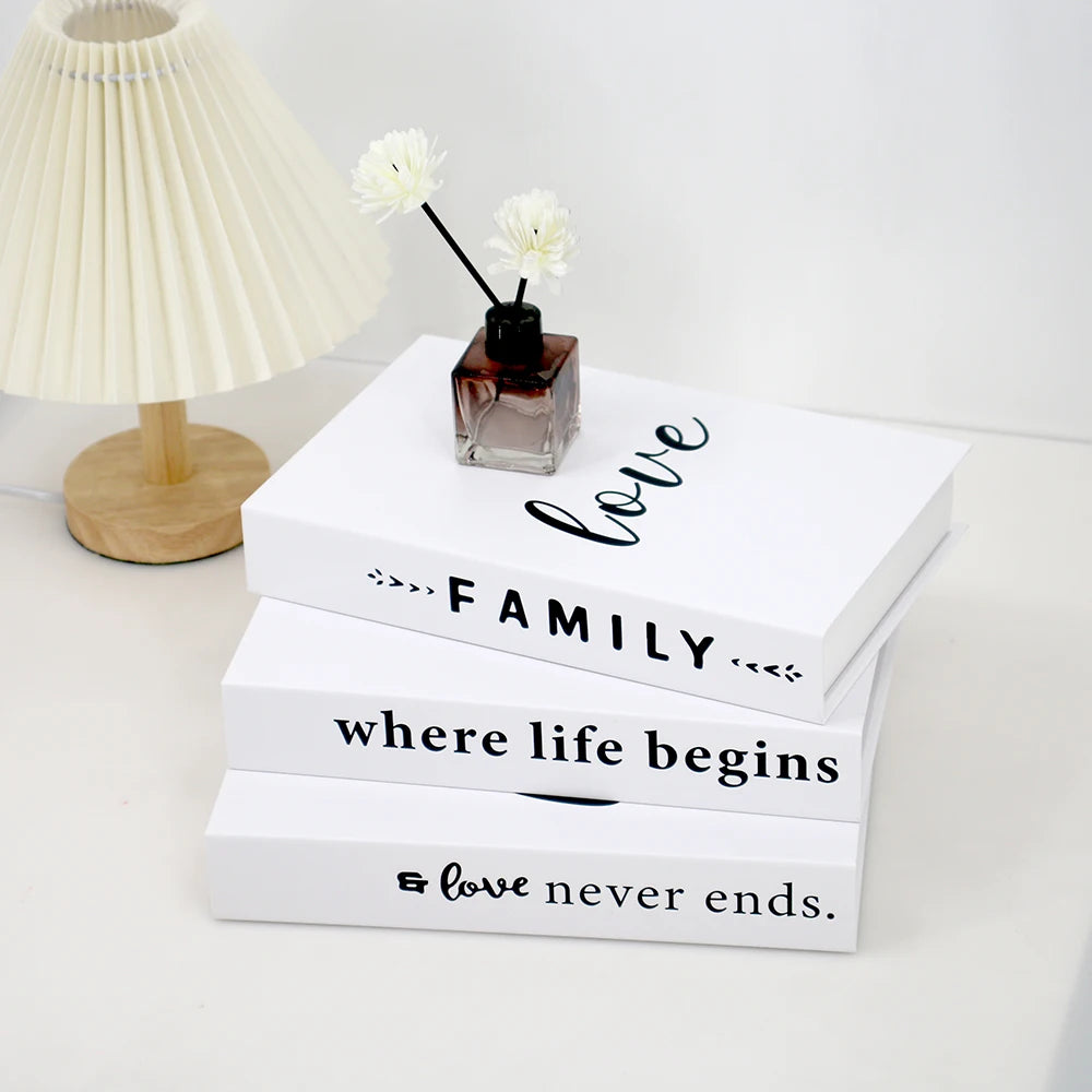 A set of three white decorative fake books with text on them, resting next to a vase of white flowers.