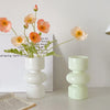 A glass flower vase holds several pink and orange-toned flowers against a white background.