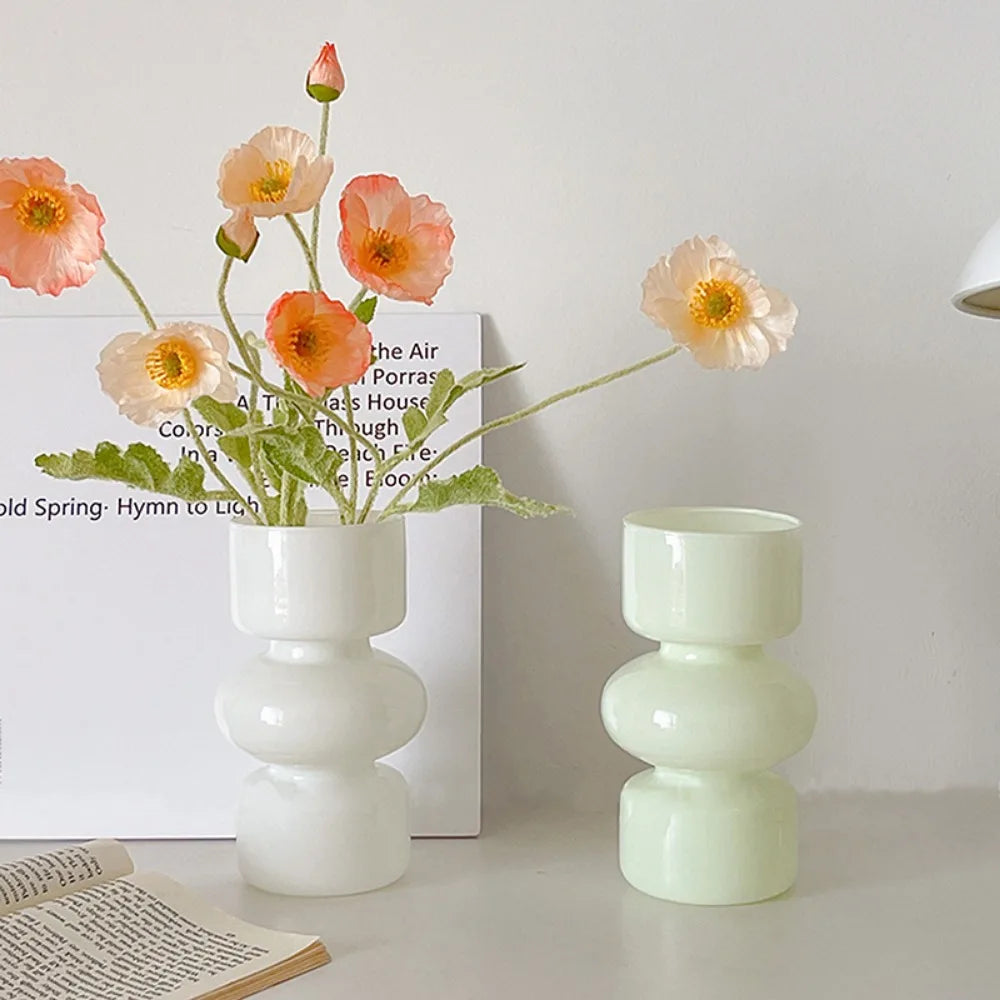 A glass flower vase holds several pink and orange-toned flowers against a white background.