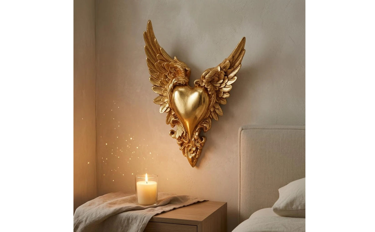 Ornate winged heart wall decor made of gold-toned metal mounted on a neutral wall.