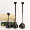 A set of three black waterdrop design candle holders standing upright on a white surface.