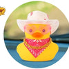 A yellow rubber duck with a pink cowboy hat and a red bandana decoration on a dashboard.