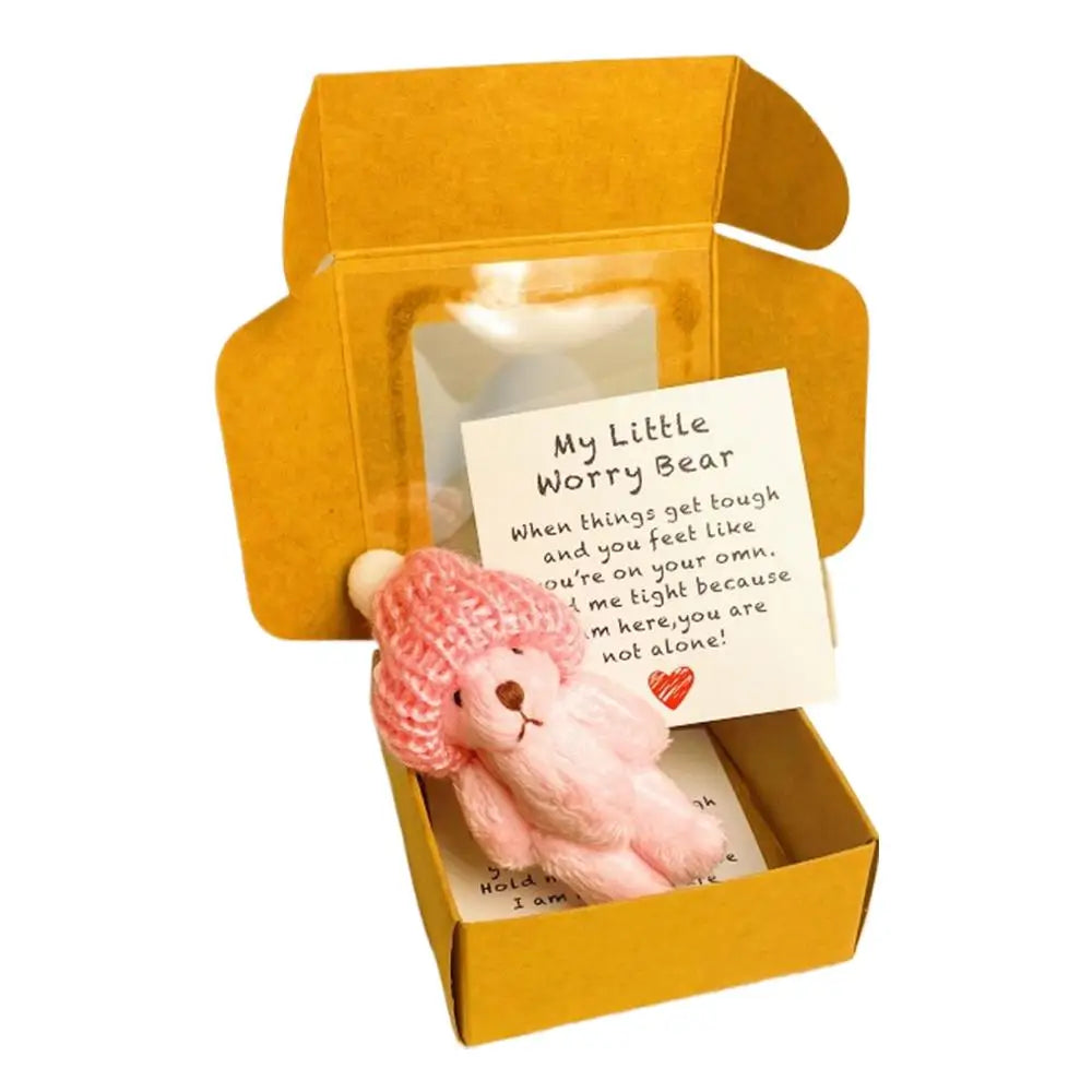 Un pequeño oso de peluche rosa y una tarjeta de inspiración empaquetados en una caja de regalo amarilla.