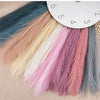 A collection of artificial pampas grass stems in various shades of pink, beige, and gray displayed on a wooden surface.