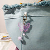 A pink butterfly pendant keychain set with pearl beads hanging from a silver clasp against a light blue fabric background.