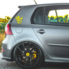 A gray car with a yellow patriotic skull decal on the rear fender and black aftermarket wheels.