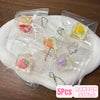 Five clear plastic pouches containing cute cartoon food squeeze toys or keychains on a white plate