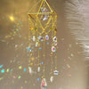 A gold crystal hanging suncatcher decoration featuring a crescent moon and various colored crystals.