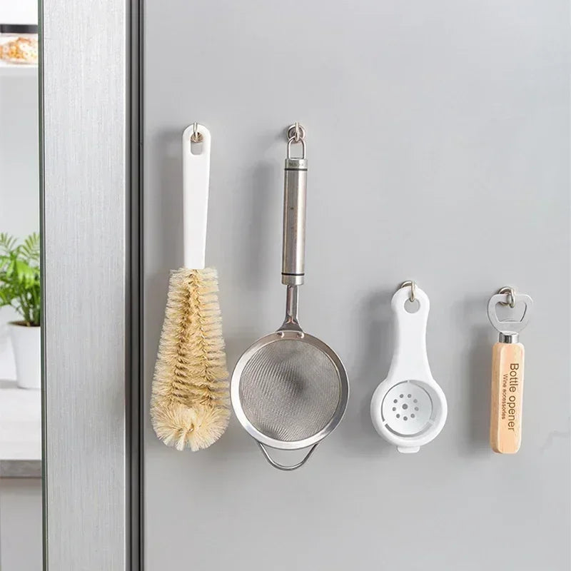 Stainless steel magnetic hooks hanging on a door or cabinet, including a whisk and a bottle opener.