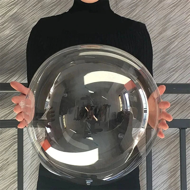 A person holds a large, clear inflatable balloon against a gray textured background.