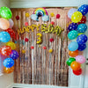 A metallic tinsel foil fringe curtain backdrop for parties featuring balloons and a happy birthday sign.