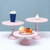 A pink metal cake stand displaying a pastry and a blue cup on a light blue background.