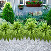 Two large artificial Boston ferns displayed in a garden setting with flowers and greenery.