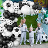 A family of three children playing with a large black and white soccer ball in front of a green backdrop decorated with ballo