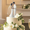 Elegant wedding cake topper featuring a bride and groom in white attire surrounded by white flowers