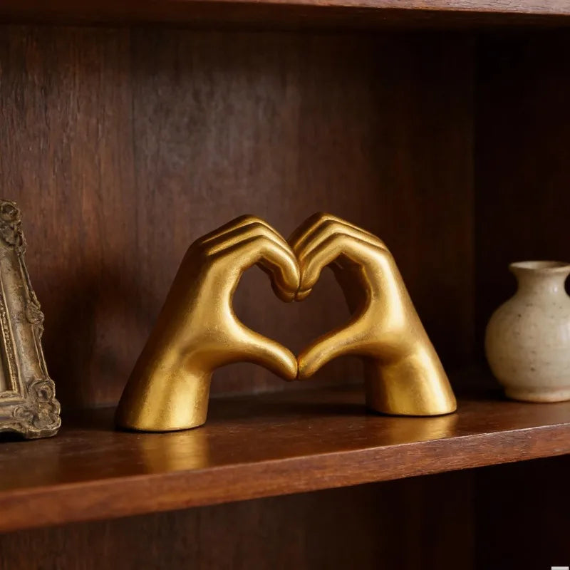 A golden sculpture of two hands forming a heart, displayed on a wooden shelf.