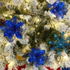 A close-up of a Christmas tree decorated with blue and white silk artificial flowers and gold sparkle accents.