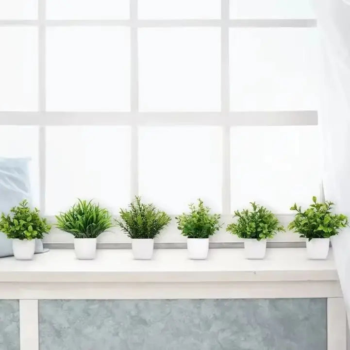 A row of small green artificial bonsai plants with eucalyptus accents displayed on a white windowsill.