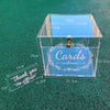 A clear acrylic gift box with a lid, featuring engraved text and decorative elements on a green surface.