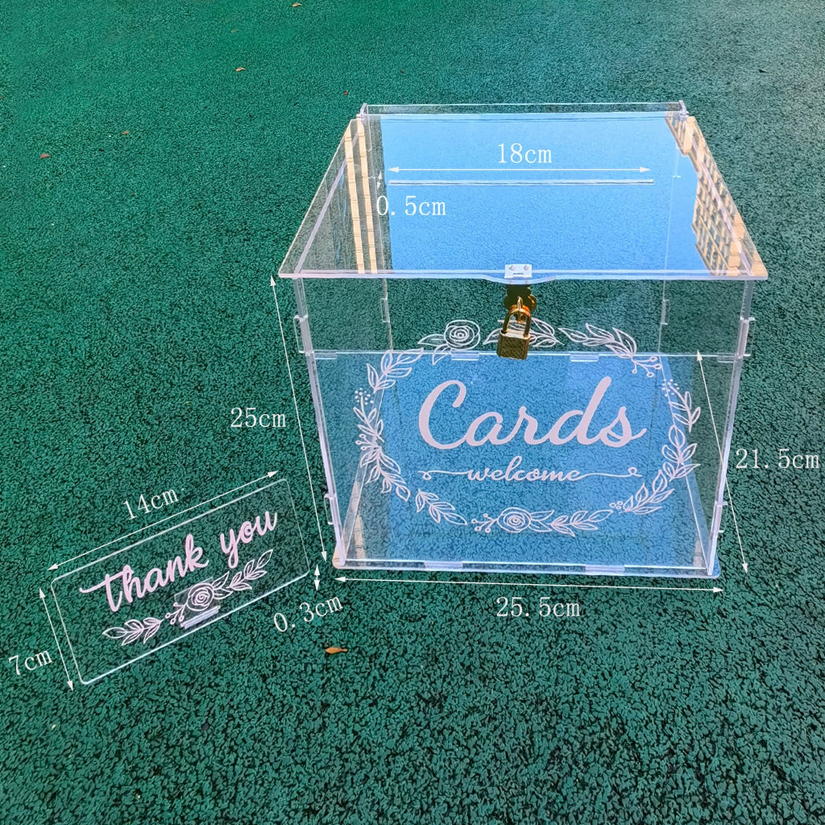 A clear acrylic gift box with a lid, featuring engraved text and decorative elements on a green surface.