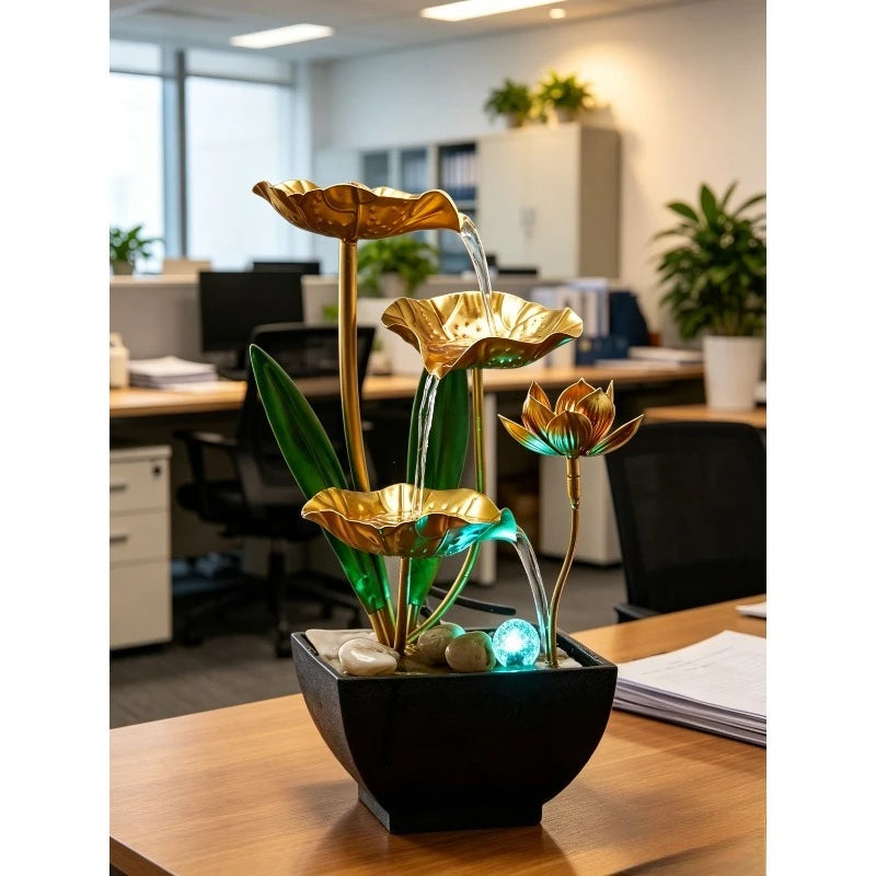 A golden lotus water fountain with green leaves and blue LED lighting sits in a black pot on a wooden table.