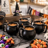 Black witch cauldron mugs filled with orange liquid served on a dark table with Halloween treats