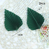 Two dark green palm leaf cake toppers with a pleated design shown on a white mesh background.