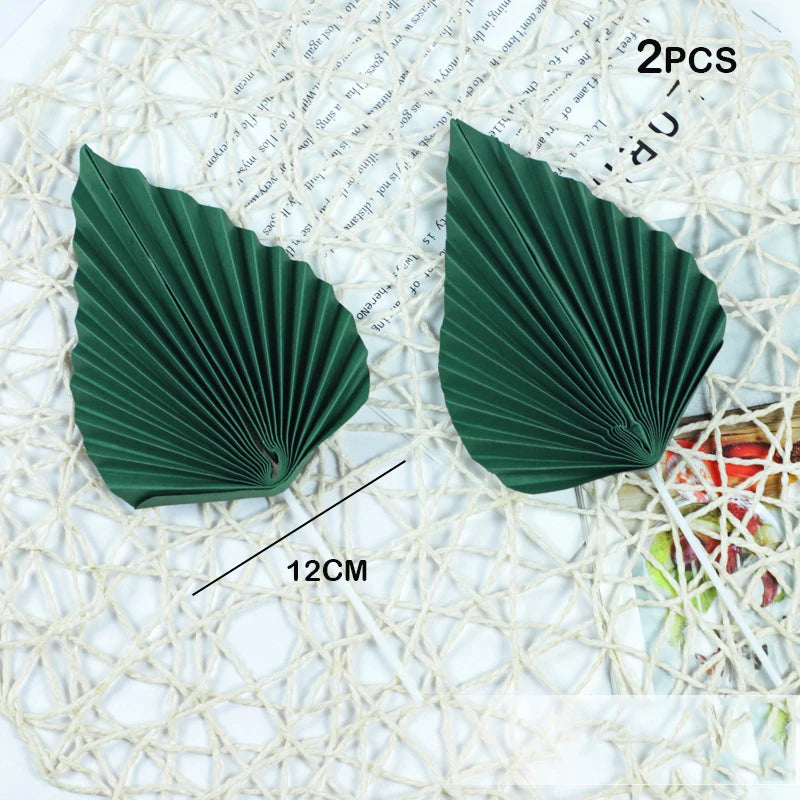Two dark green palm leaf cake toppers with a pleated design shown on a white mesh background.
