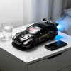 A black remote control car model is displayed on a white surface next to a glass and a smartphone.