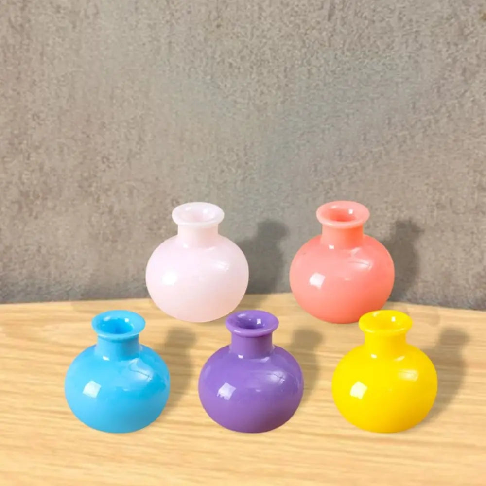 A collection of five miniature resin vases in pink, orange, blue, purple, and yellow on a wooden surface.