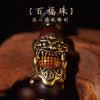 A close-up of a handcrafted Pixiu bracelet featuring a bronze-colored dragon head charm and semi-jade beads on a dark wood ba
