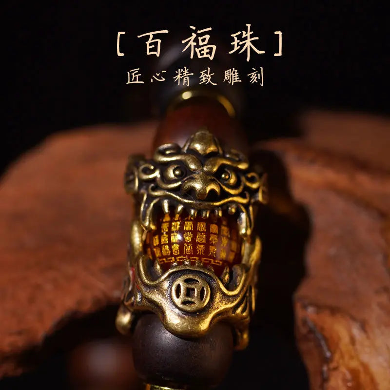 A close-up of a handcrafted Pixiu bracelet featuring a bronze-colored dragon head charm and semi-jade beads on a dark wood ba