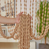 A hand is pulling a beige beaded string curtain with tassels, used as a bohemian door and window drape.