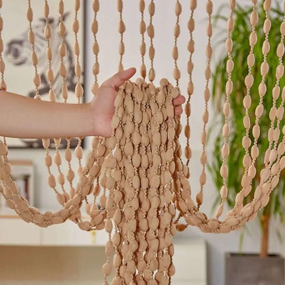 A hand is pulling a beige beaded string curtain with tassels, used as a bohemian door and window drape.