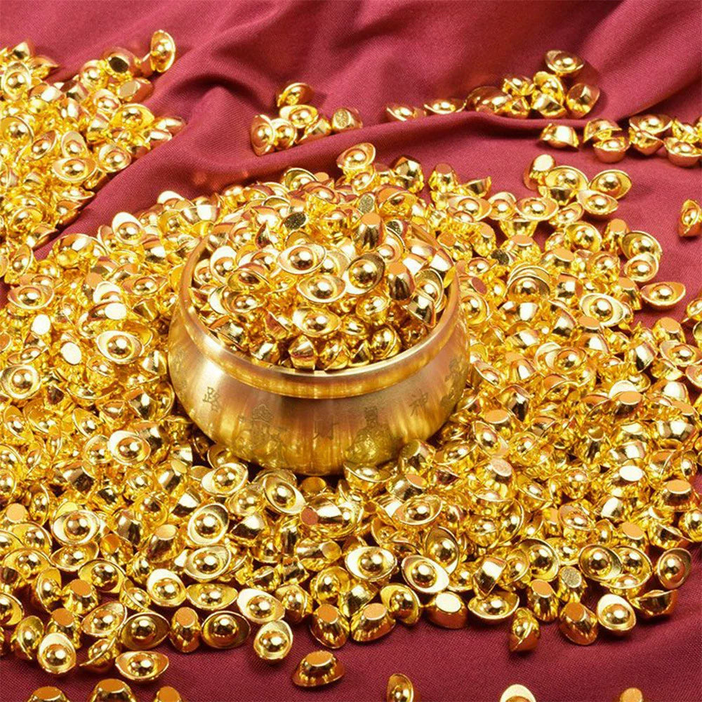 A pile of gold-colored metal prosperity decorations set resting on a deep red fabric.