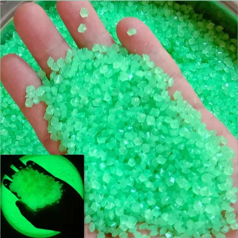 A hand holds a pile of bright green glow-in-the-dark luminous pebbles for garden and aquarium decor.