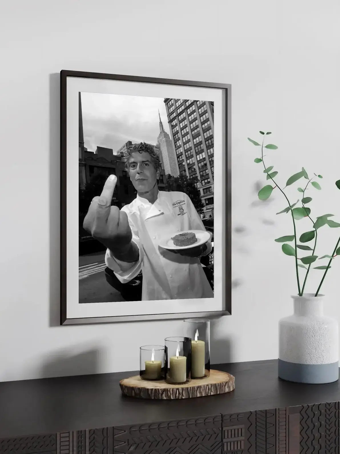 Framed black and white photograph of a man making a finger sign, displayed on a dark surface.