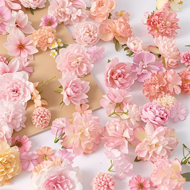 A collection of pink and peach silk artificial flower heads for crafts and decor arranged on a light brown surface.