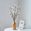 A vase holds artificial plum blossom decorations with bare branches on a white surface.