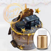 A dark chocolate cake decorated with a black car model and gold glitter dust, next to a glass bottle of gold liquid.