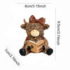 A cute coffee cow figurine with brown fur and a bow, sitting next to an open book.