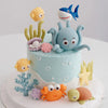 A cake decorated with ocean animal toppers including a blue whale, a gray octopus, and an orange sea turtle.