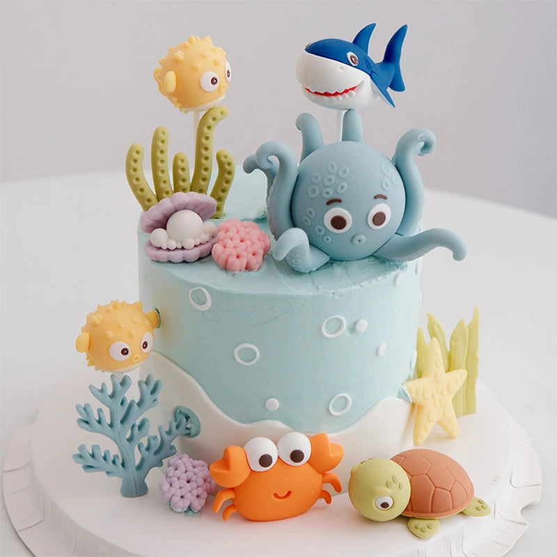 A cake decorated with ocean animal toppers including a blue whale, a gray octopus, and an orange sea turtle.
