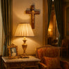 A wooden crucifix with a gold Jesus figure displayed on a bedside table in a richly decorated room.