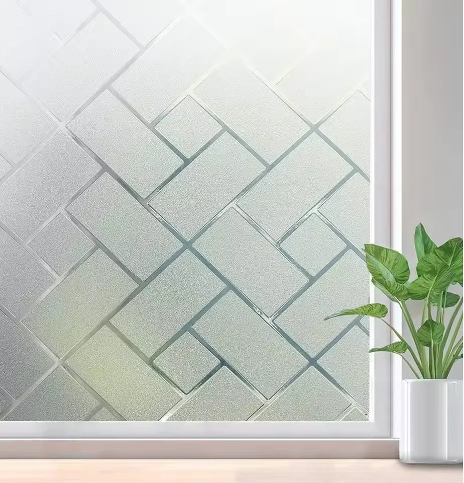 Frosted electrostatic window film applied to a glass pane, featuring a geometric pattern and a green plant in the foreground.